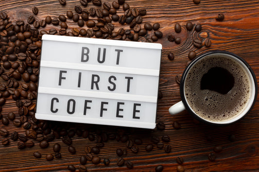 Verse koffiebonen op tafel met kopje koffie en de tekst But first coffee